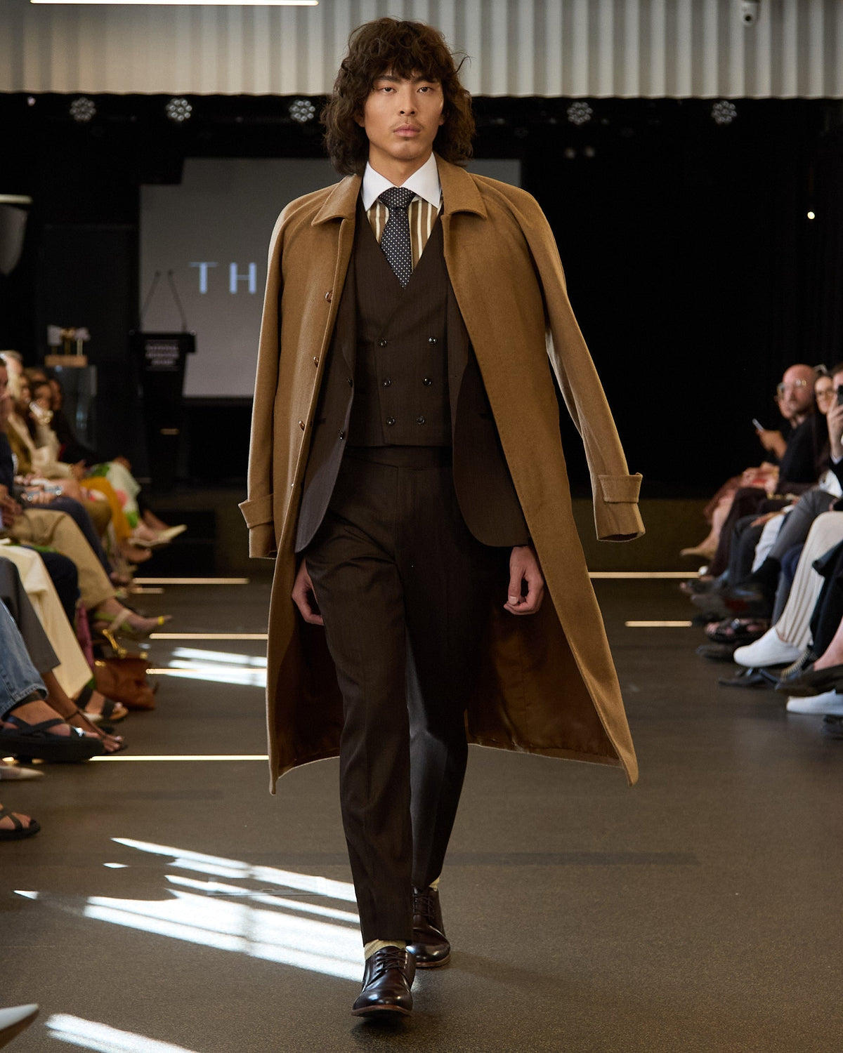 Model in a brown three-piece and camel overcoat walking the runway at Melbourne Fashion Festival