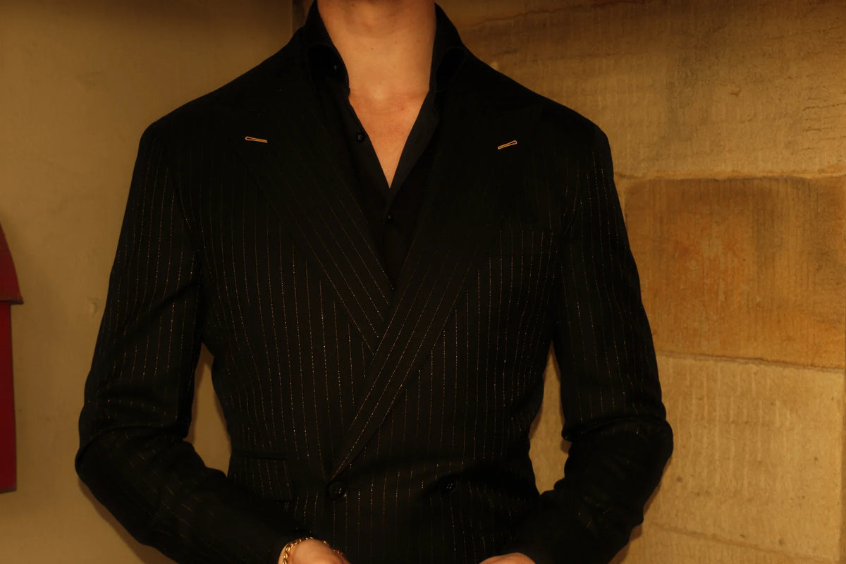 A black double-breasted jacket in Dormeuil Gold Forever, fine gold stripes catching the light