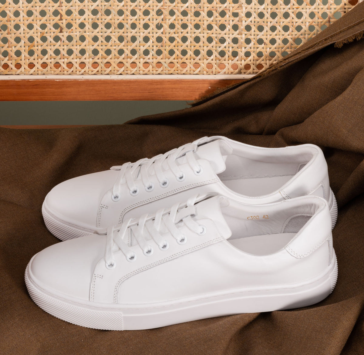 Zante White Sneaker pair displayed on a brown fabric surface with a woven cane backdrop