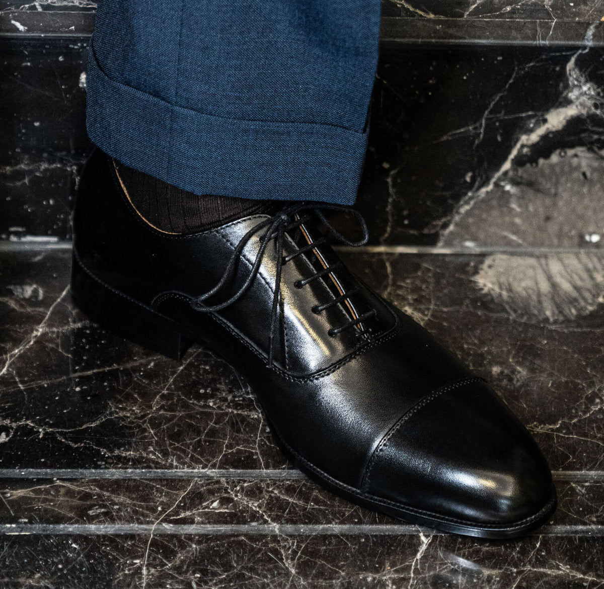 The Haider Black Leather Oxford worn on a model's foot with a cuffed trouser