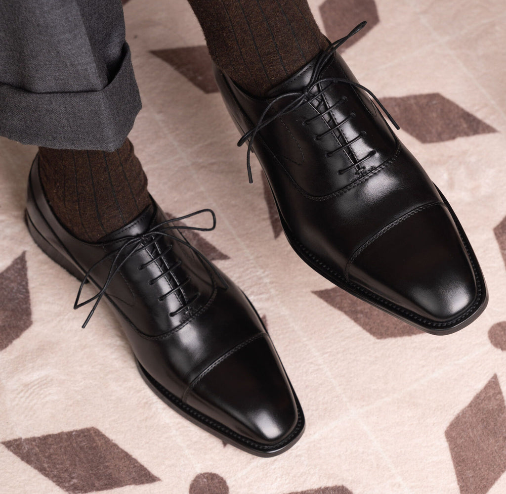 The Konbanwa Square-Toe Triple-Stitched Black Oxford shoes worn on feet with pinstripe trousers