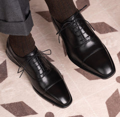 The Konbanwa Square-Toe Triple-Stitched Black Oxford shoes worn on feet with pinstripe trousers