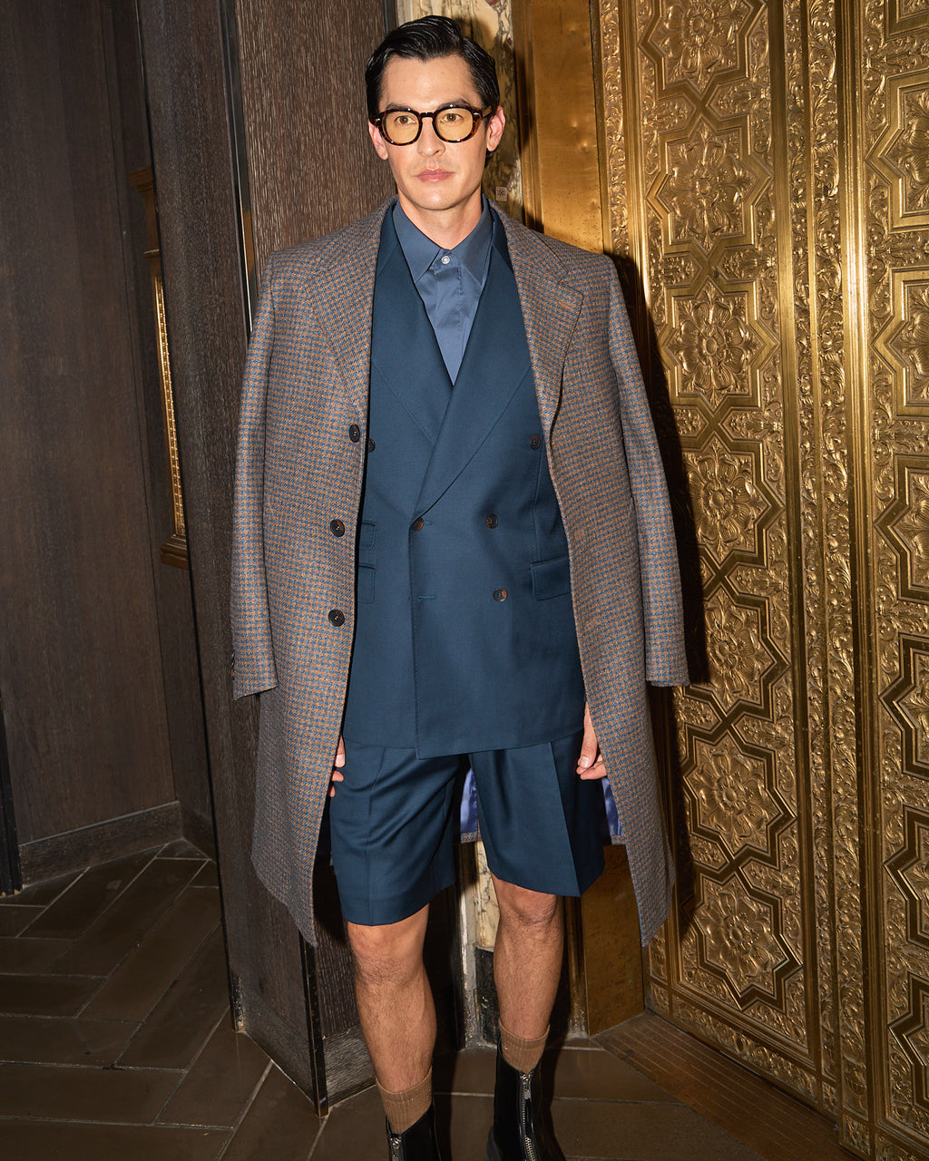 Fast Break Tailored Set with an overcoat, model with hands clasped at the same gold doorway