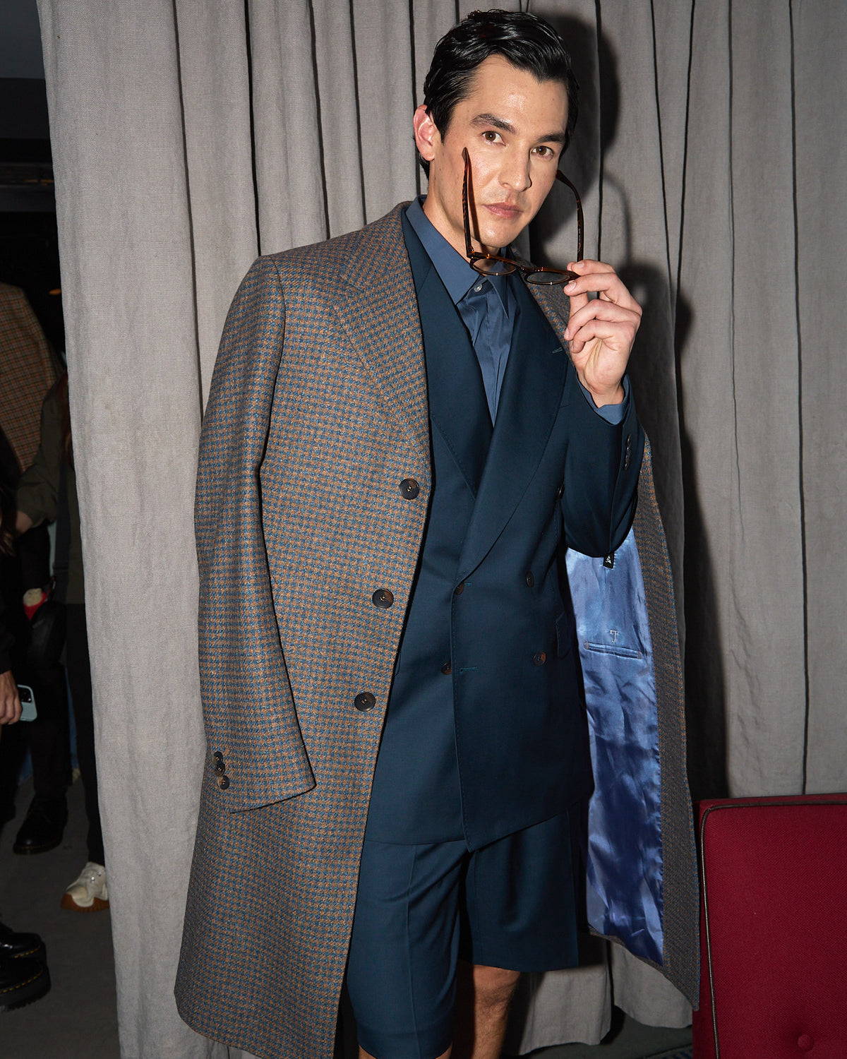 Fast Break Tailored Set with an overcoat, model adjusting sunglasses by a curtain