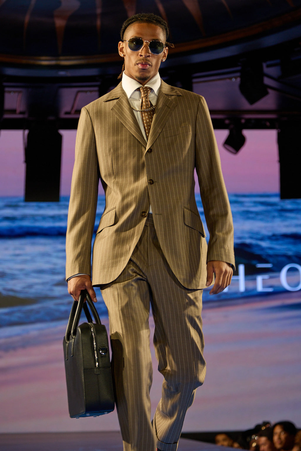 Beige Pinstripe Suit, a model walks the runway toward camera holding a black leather bag
