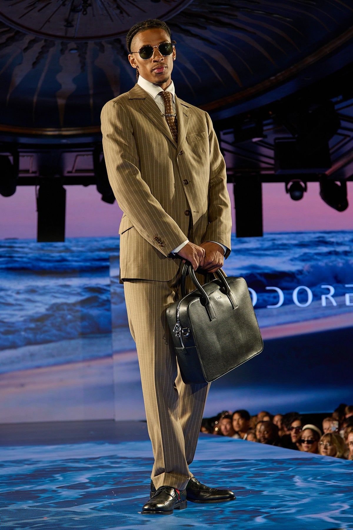 Beige Pinstripe Suit, closer runway shot of a model gripping the bag in both hands
