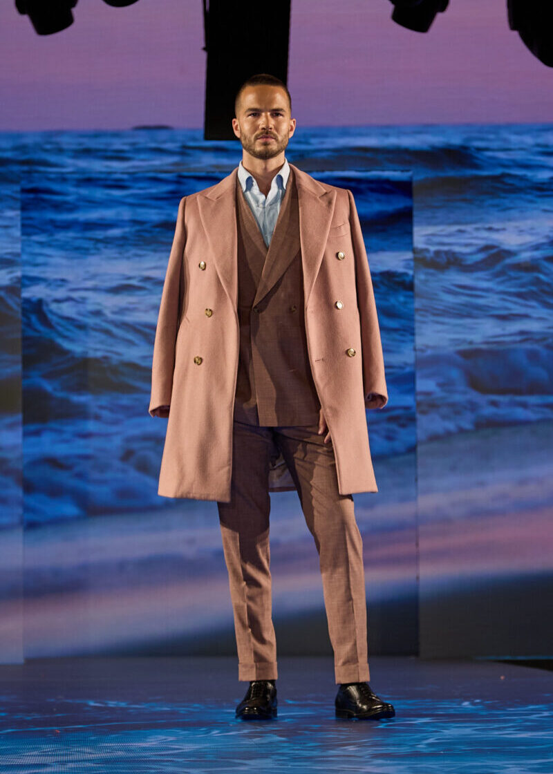 Rosewood Overcoat, a model stands still on the runway against an ocean-themed backdrop
