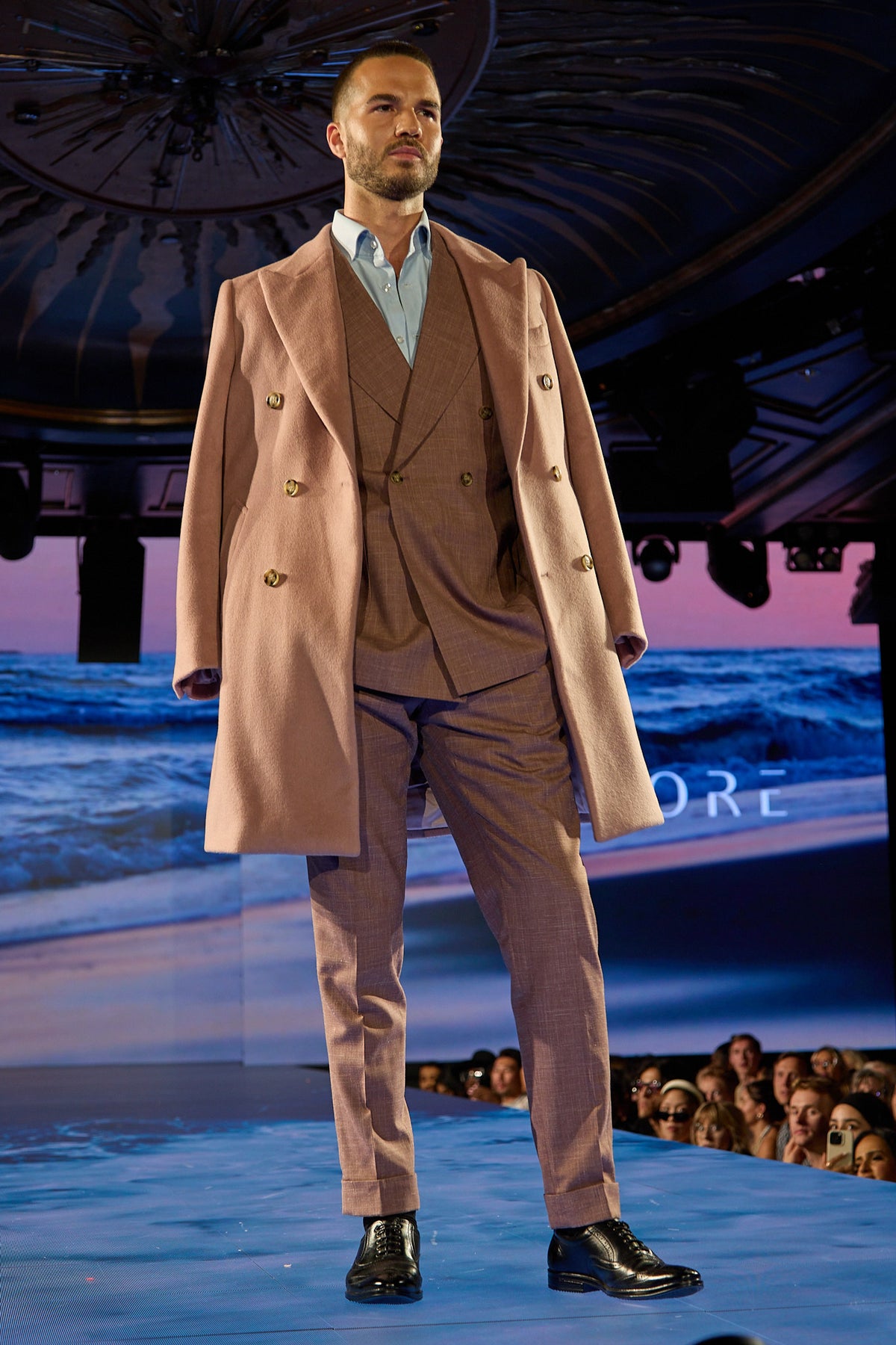 Dusty Rose Suit with its overcoat, full-length runway shot against an ocean backdrop
