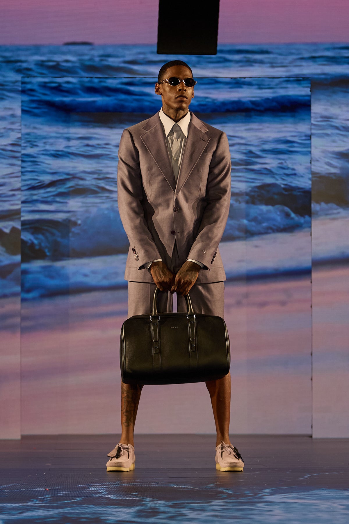 Lavender Haze Suit, a model stands front-on holding the duffel bag with both hands