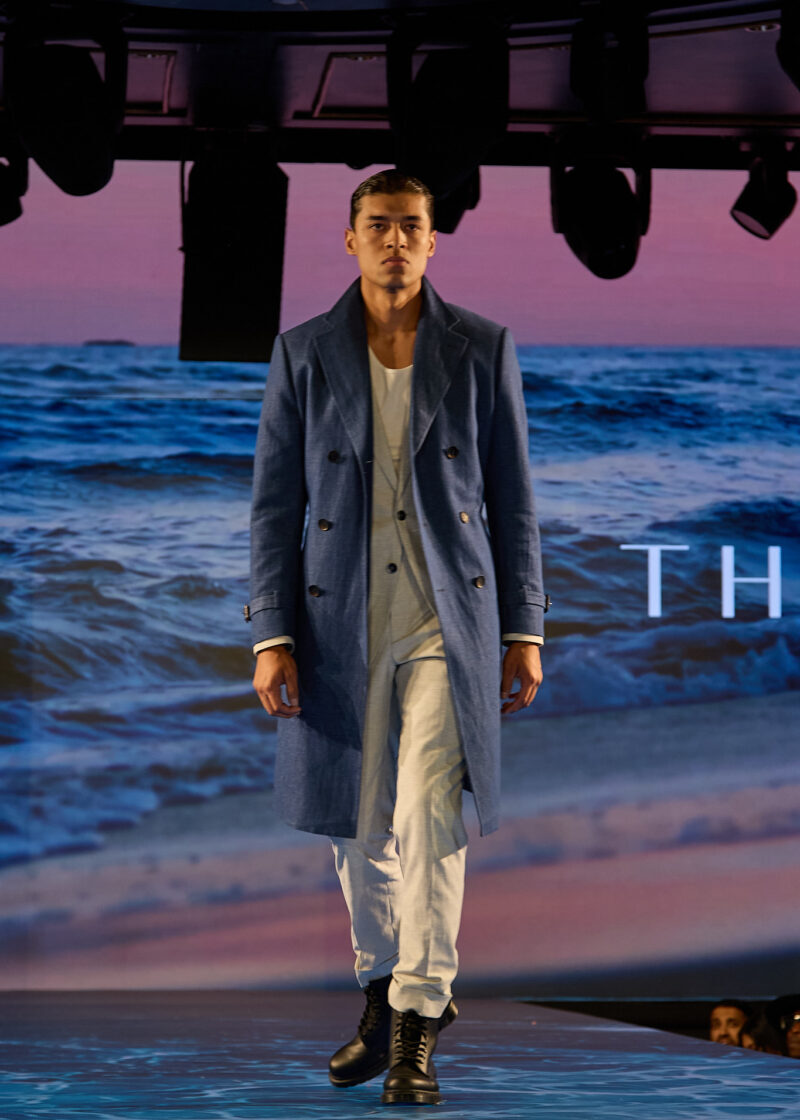Grey Jersey Stretch Suit styled with an overcoat, runway shot against an ocean backdrop