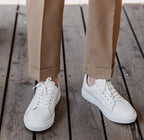 Zante White Sneaker worn by a model with camel trousers, standing on a wooden deck