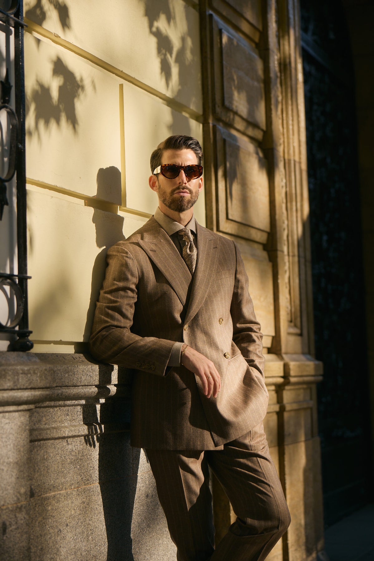 Langley brown pinstripe suit on a model leaning against a sunlit wall