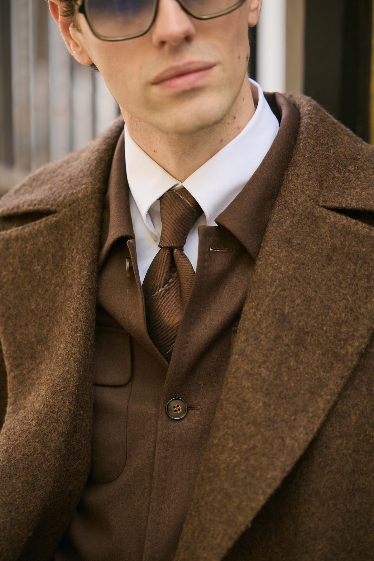 The Beaumont Brown Overcoat, closer face-and-collar crop with sunglasses and a tie