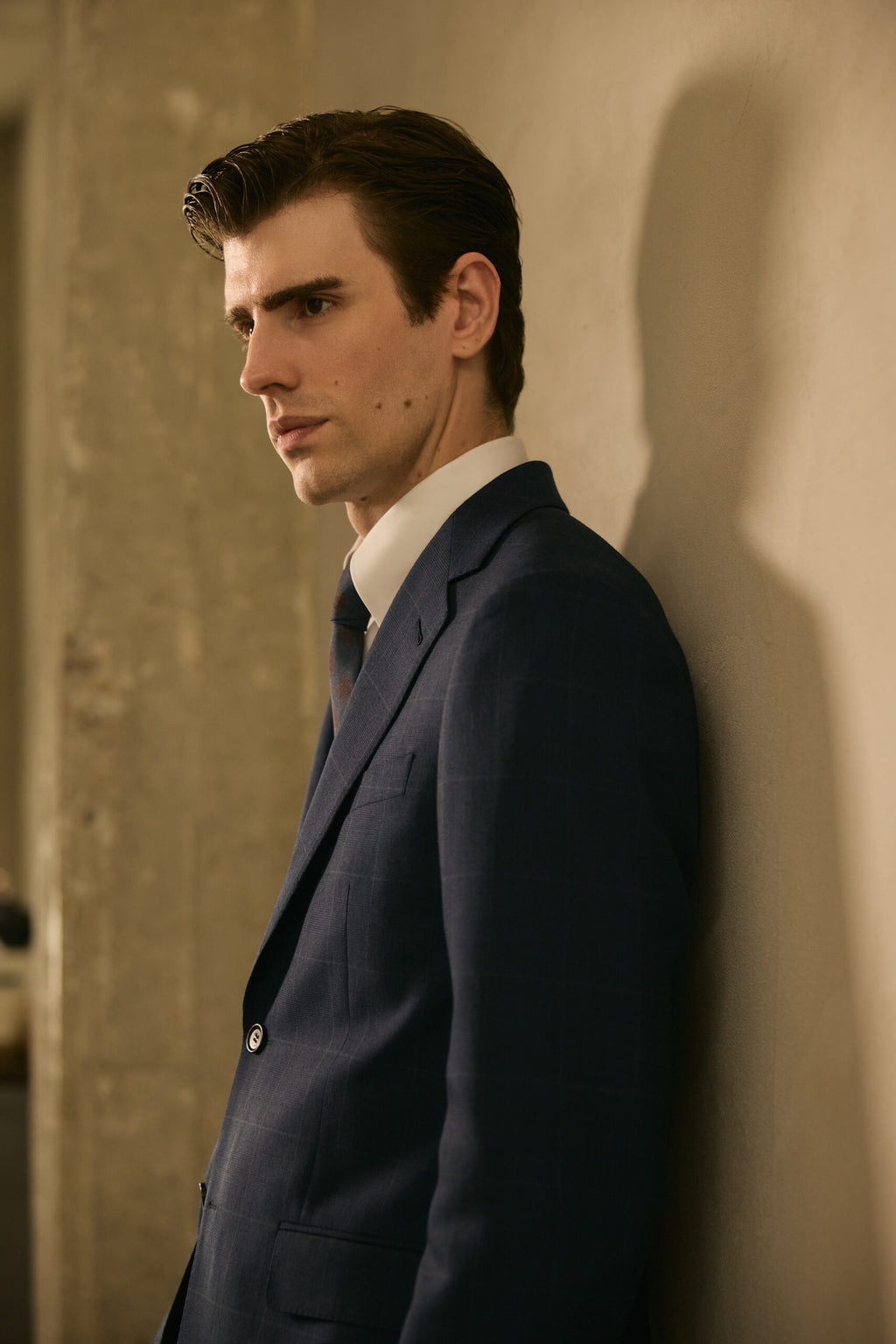 The Stratford Navy Check Suit worn by a model in side profile against a wall