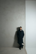 The Ellison Tech Navy Coat worn full-length, leaning against a wall