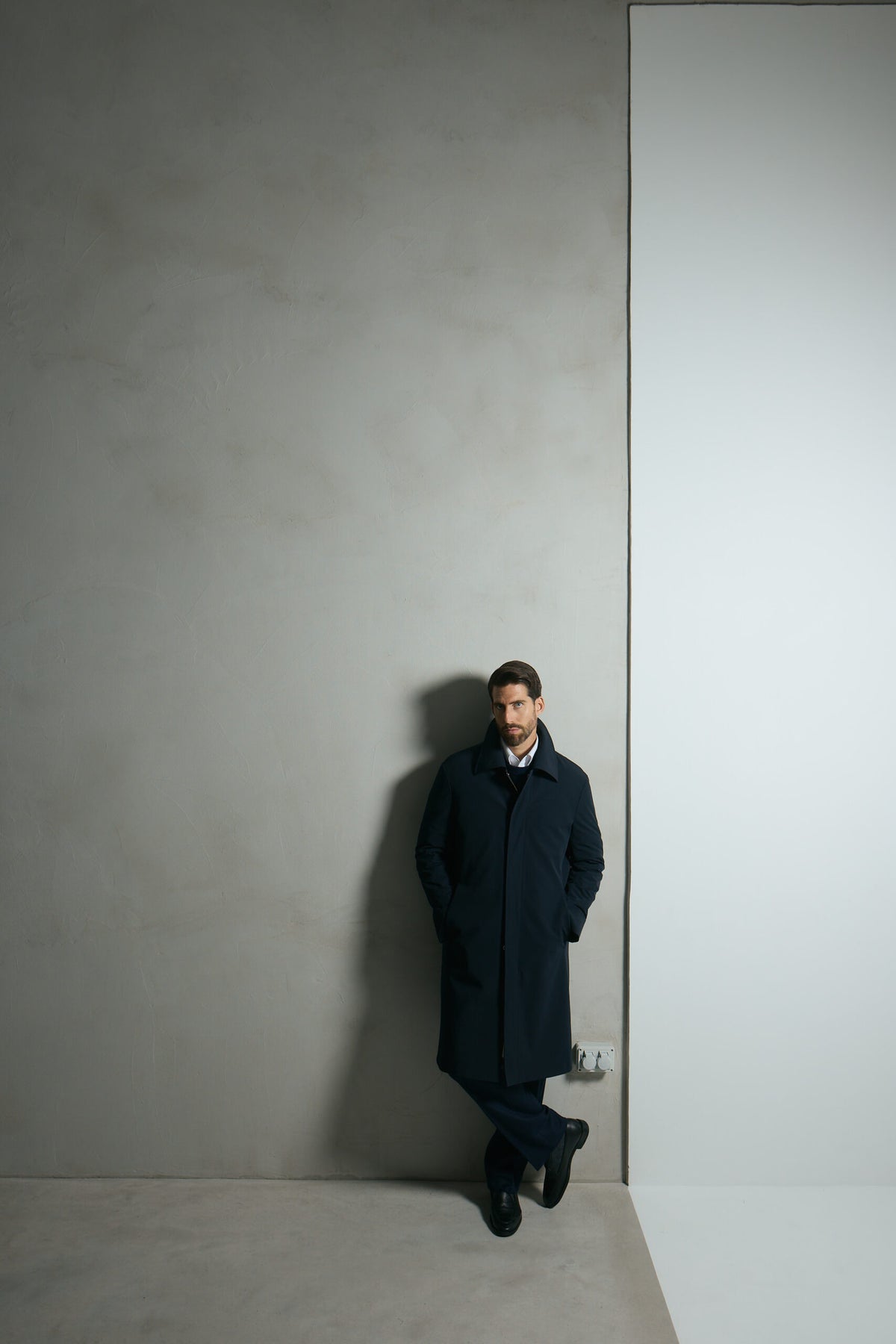 The Ellison Tech Navy Coat worn full-length, leaning against a wall