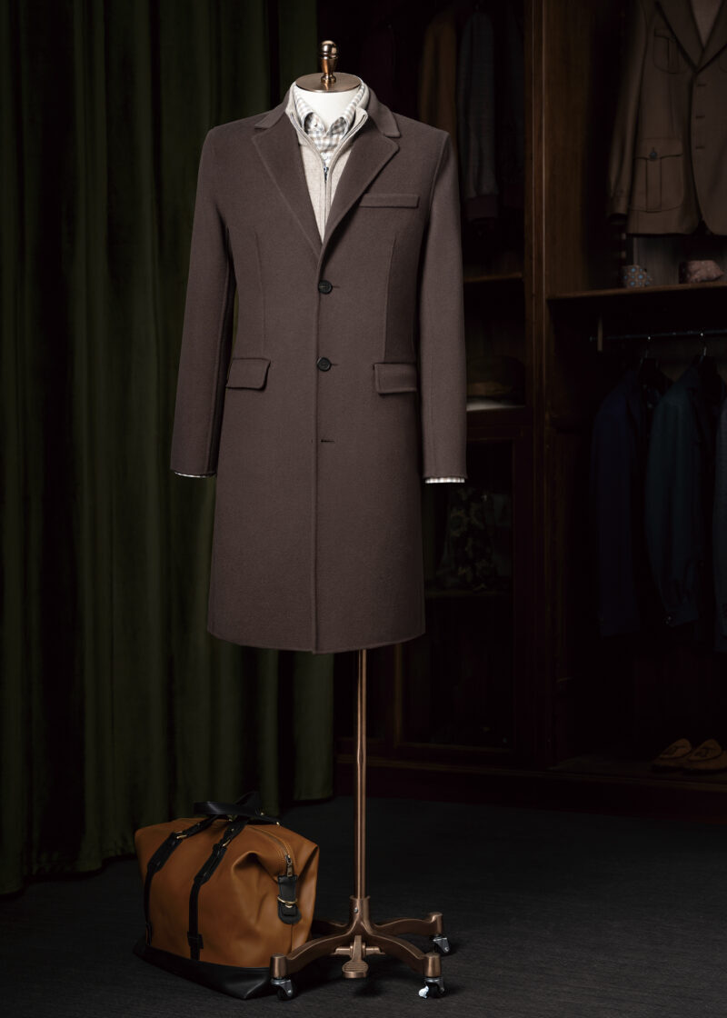 Baker Street Coffee Cashmere Blend Overcoat on a stand beside a tan duffel bag