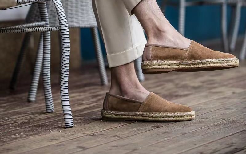 Aries Taupe Handcrafted Woven Fisherman Shoes worn on a model beside a wicker chair