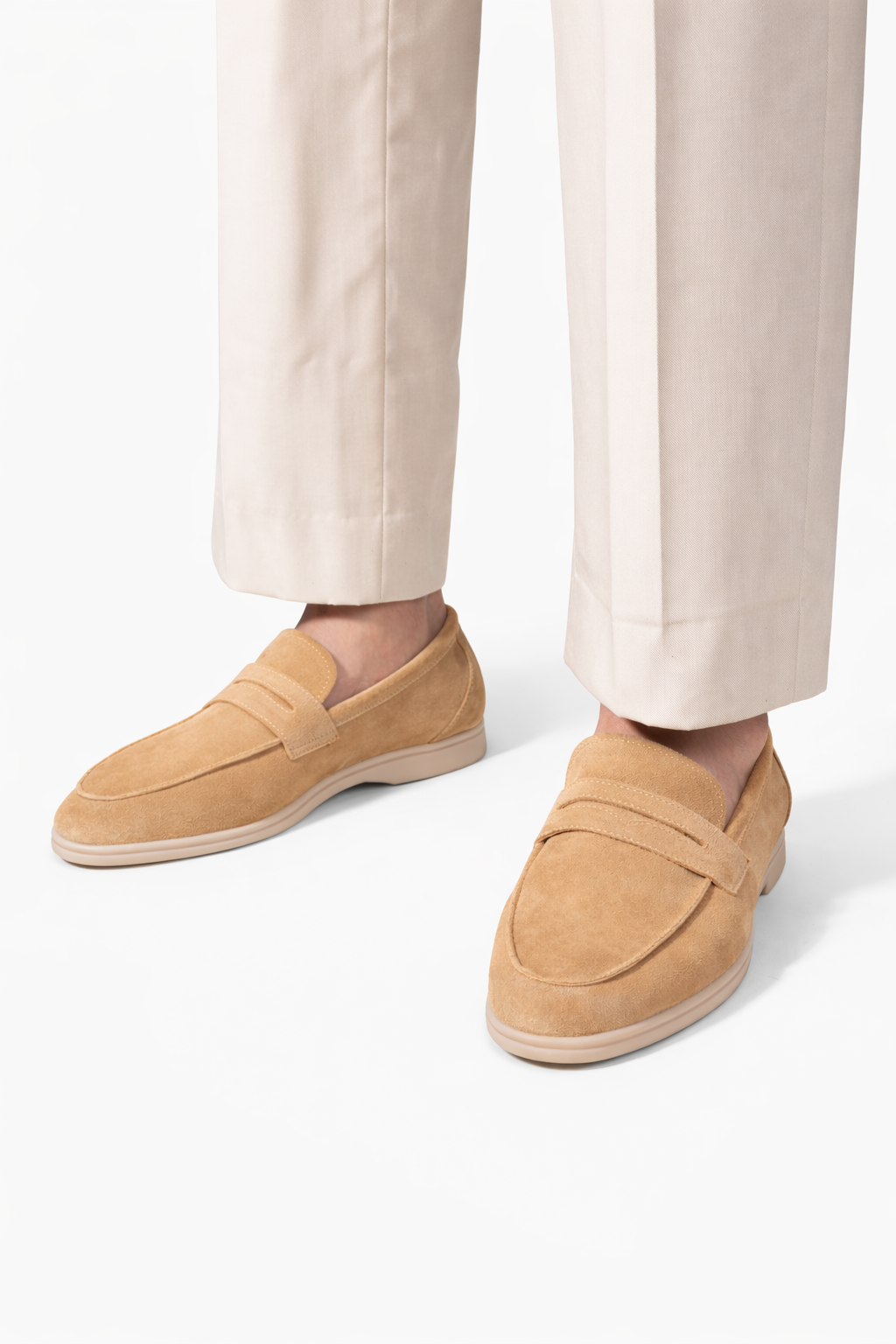 The Echelon Beige Suede Penny Loafer worn on a model's feet with cream trousers