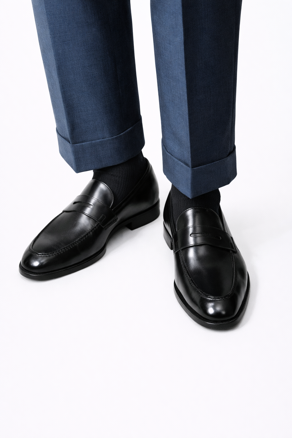 The Morton Black Leather Penny Loafer worn by a model, close-up with cuffed navy trousers