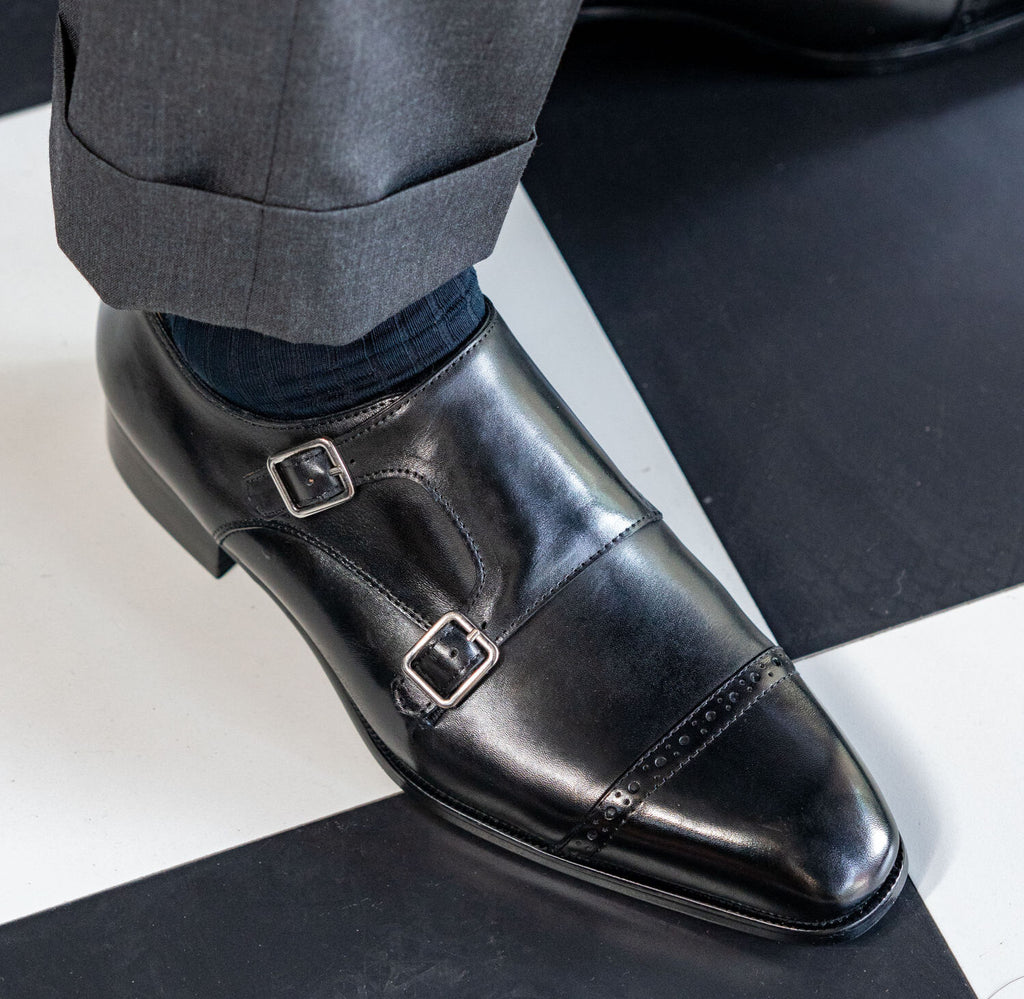 The Friar Black Leather Double Monk worn on a model's foot on a checked floor
