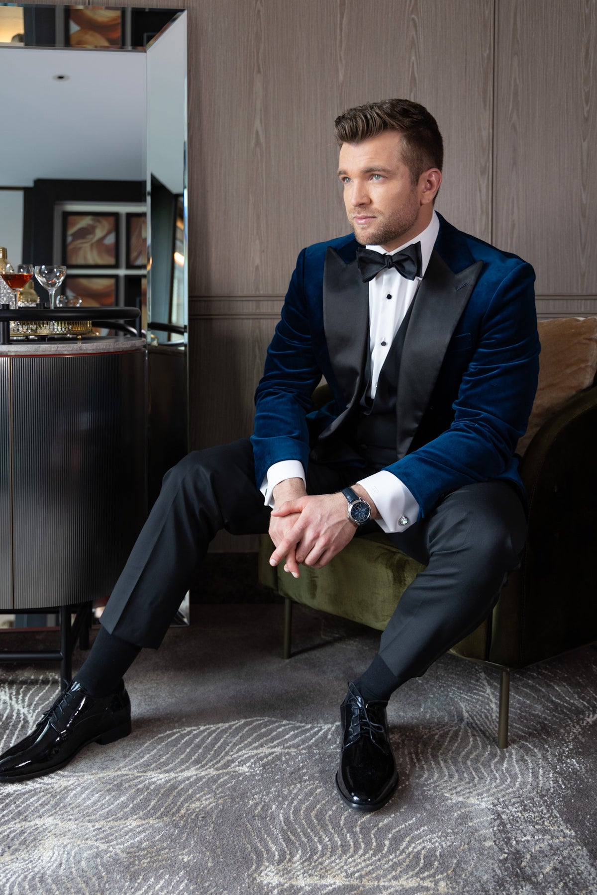 Velvet Noir navy tuxedo worn on a model seated on an ottoman