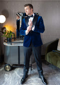 Velvet Noir navy tuxedo worn on a model adjusting his cufflink by a bar cart