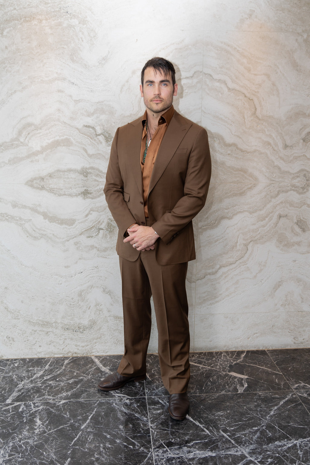 Modern Mellow brown suit on a model standing against an indoor marble wall