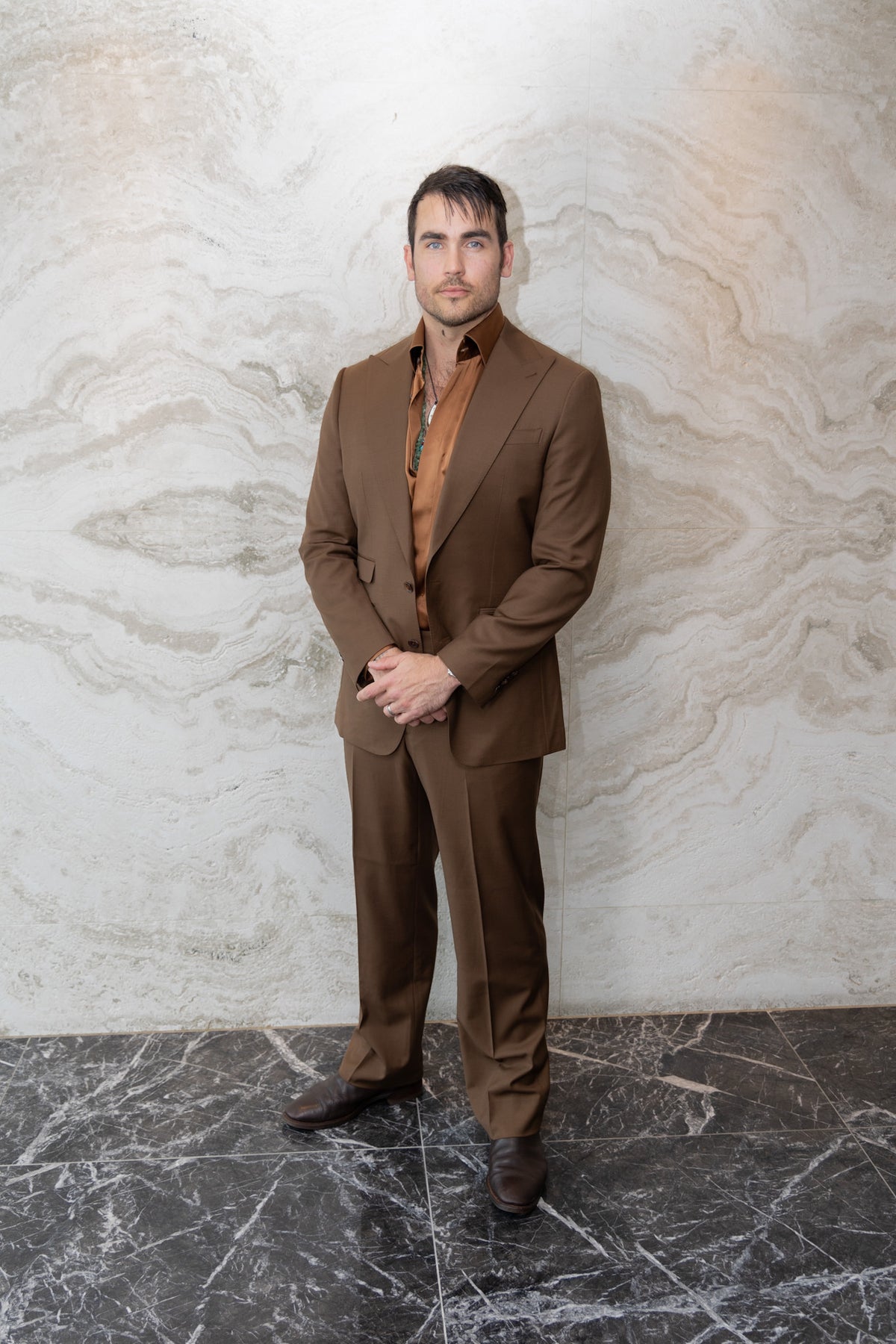 Modern Mellow brown suit on a model standing against an indoor marble wall