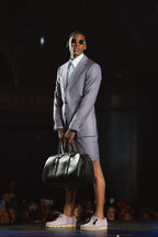 Lavender Haze Suit, a model stands in sunglasses holding a black duffel bag, dark backdrop