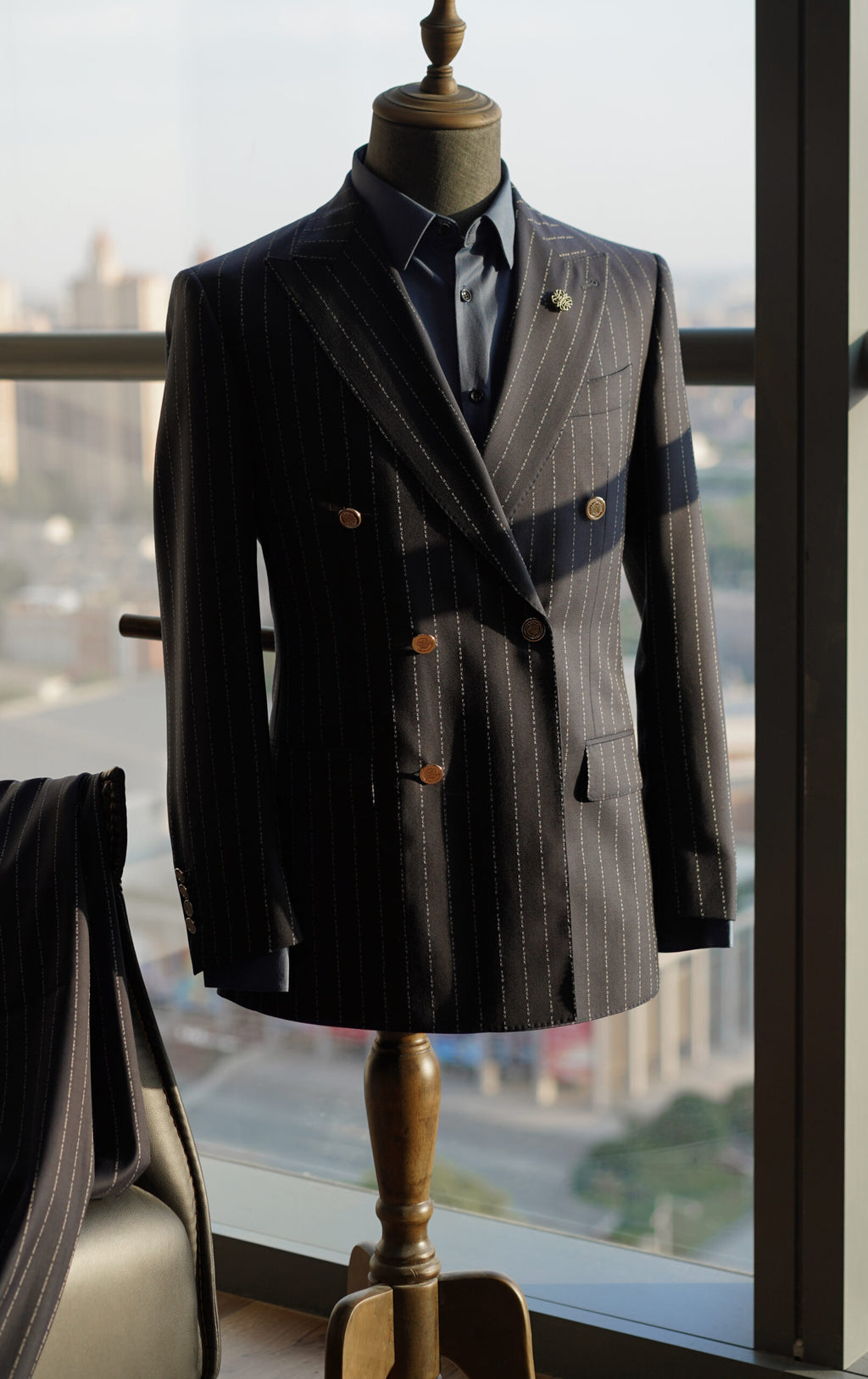The No Filter Navy Pinstripe Suit jacket on a mannequin with a lapel pin, city skyline background