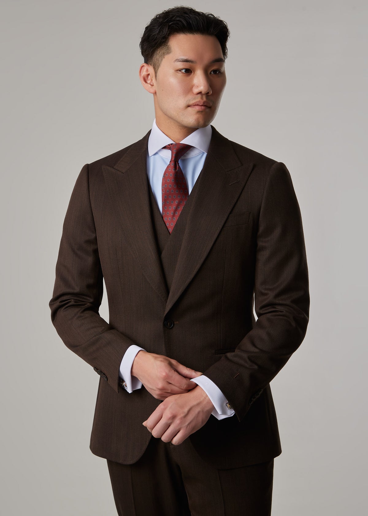 Lexington Brown Suit, torso crop on a model with hands clasped, gaze to the side