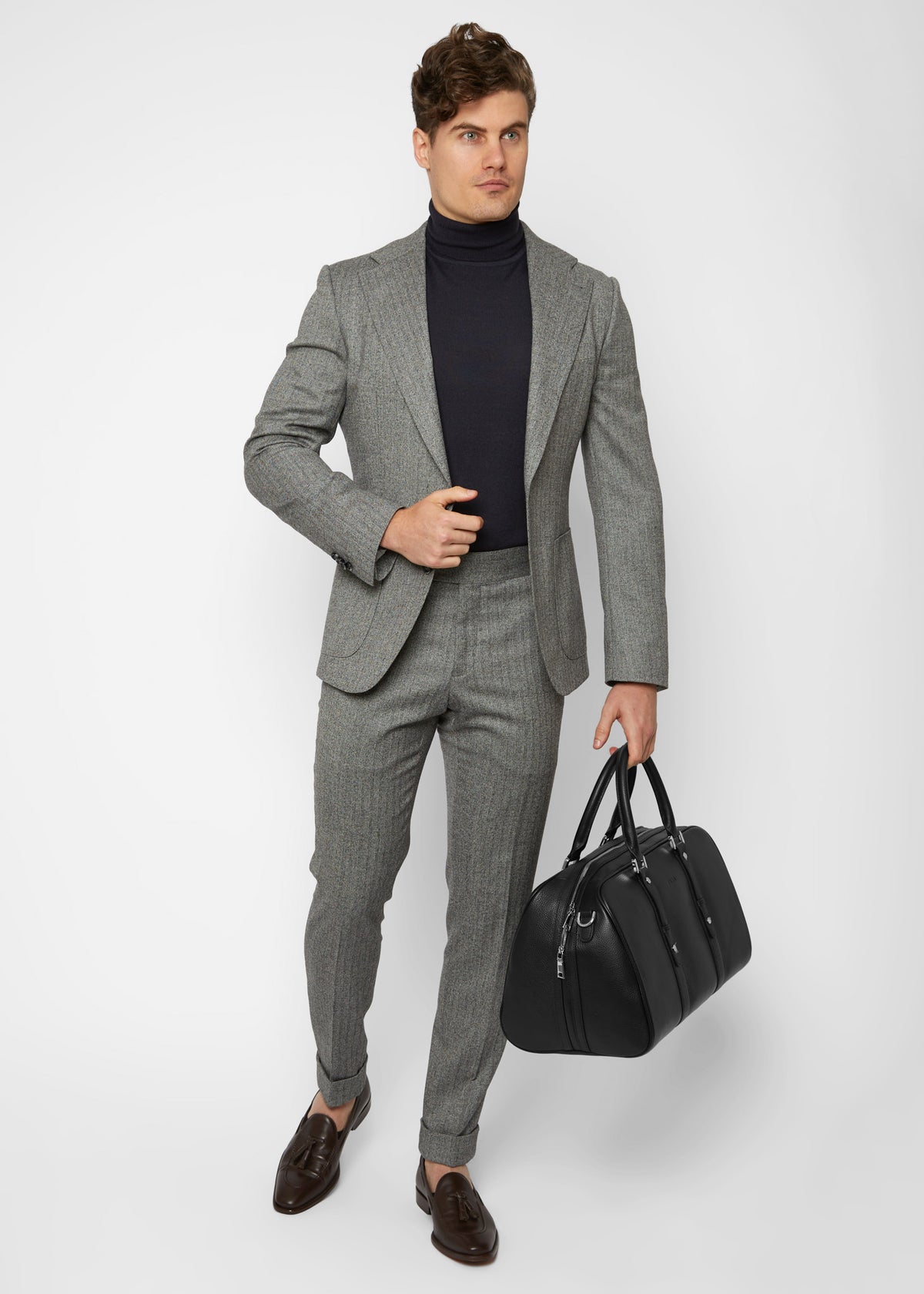 Christian travel bag carried by a model in a grey suit and turtleneck