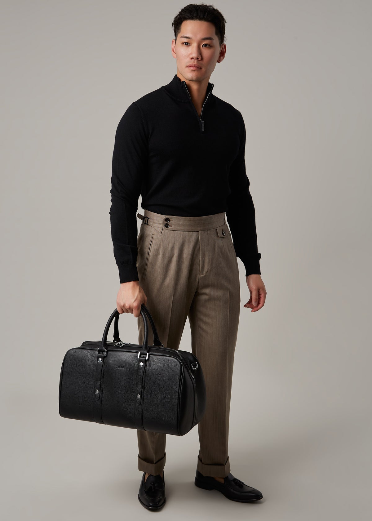 Christian travel bag held by a model wearing a black quarter-zip jumper