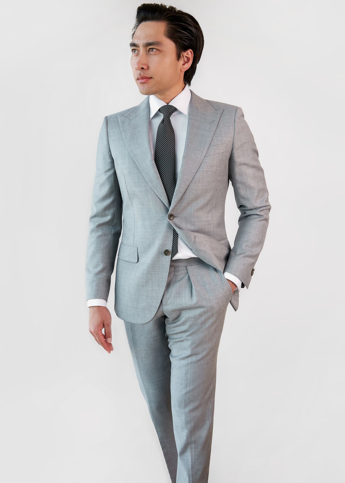The Brewhouse Light Grey Suit buttoned with a polka dot tie, model walking with hand in pocket