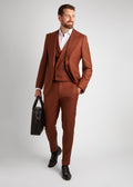Birmingham Tobacco Brown Suit, a model walks while holding a black bag, smiling