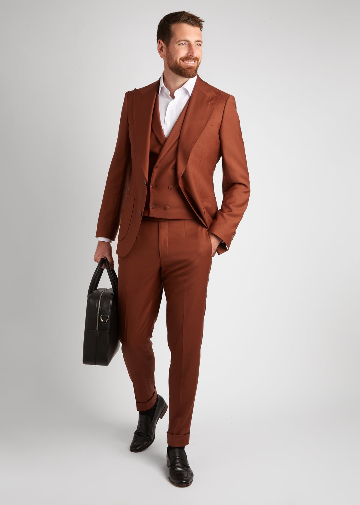Birmingham Tobacco Brown Suit, a model walks while holding a black bag, smiling