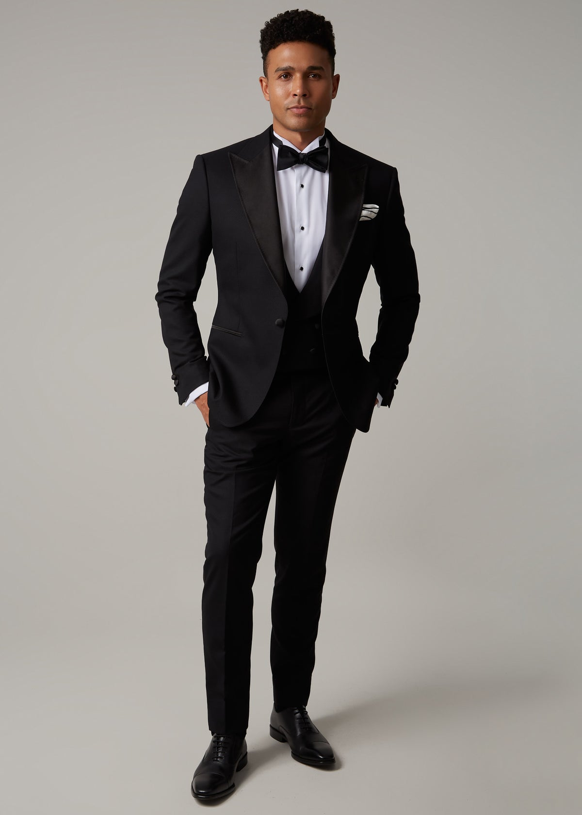 The Great Black Tuxedo jacket buttoned, full front view on a model with hands in pockets