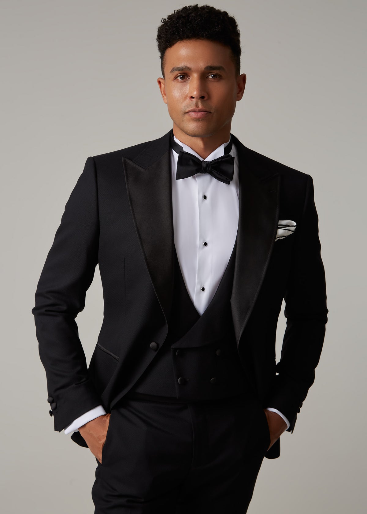 The Great Black Tuxedo jacket open over waistcoat, front view from the waist up with hands in pockets