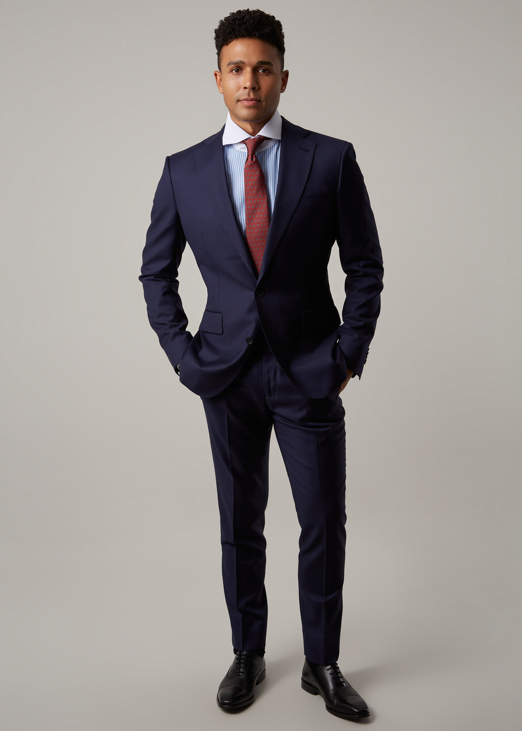 Rialto Royale Navy Suit worn with a rust tie and striped shirt, hands in pockets