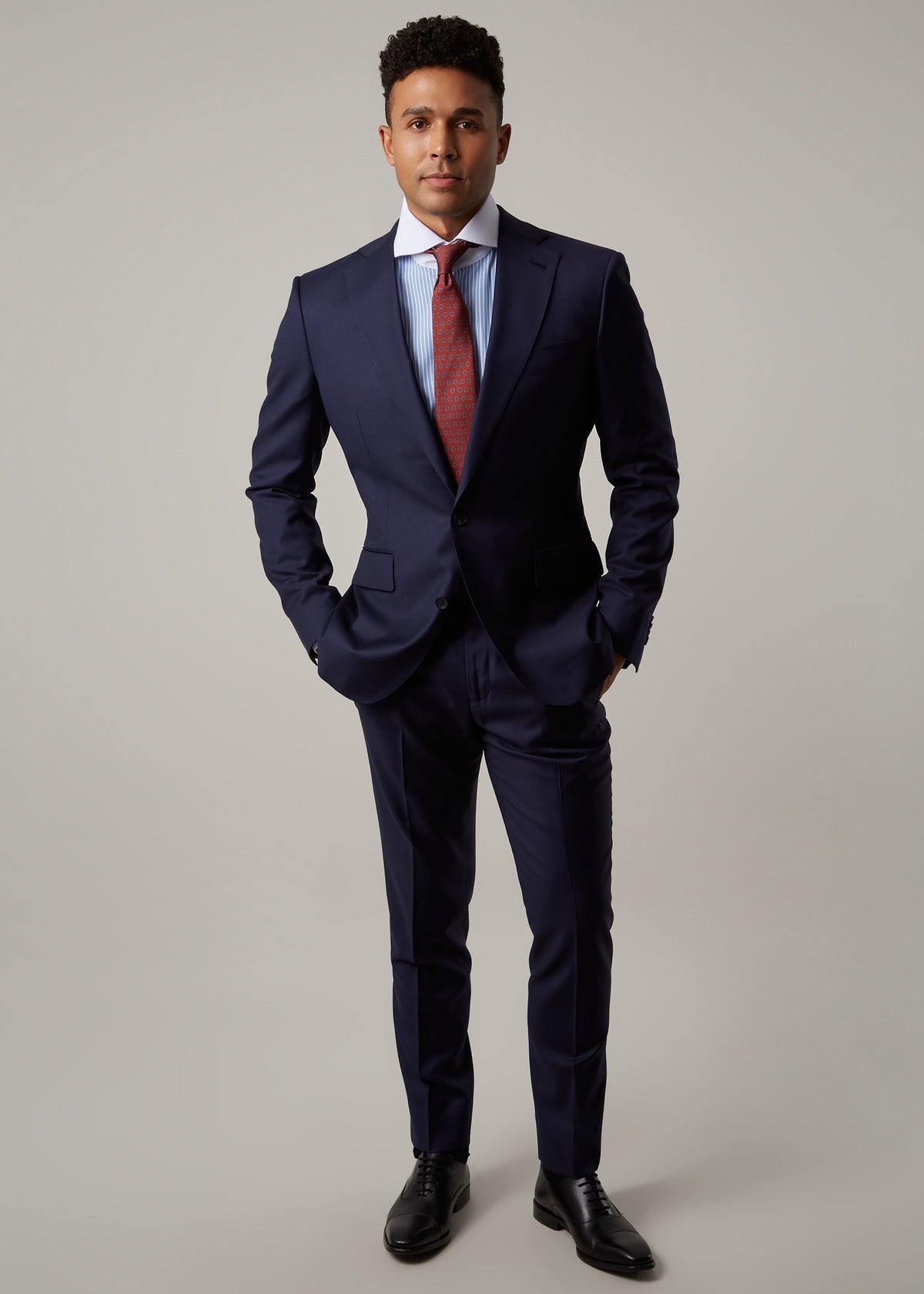 Rialto Royale Navy Suit worn with a rust tie and striped shirt, hands in pockets