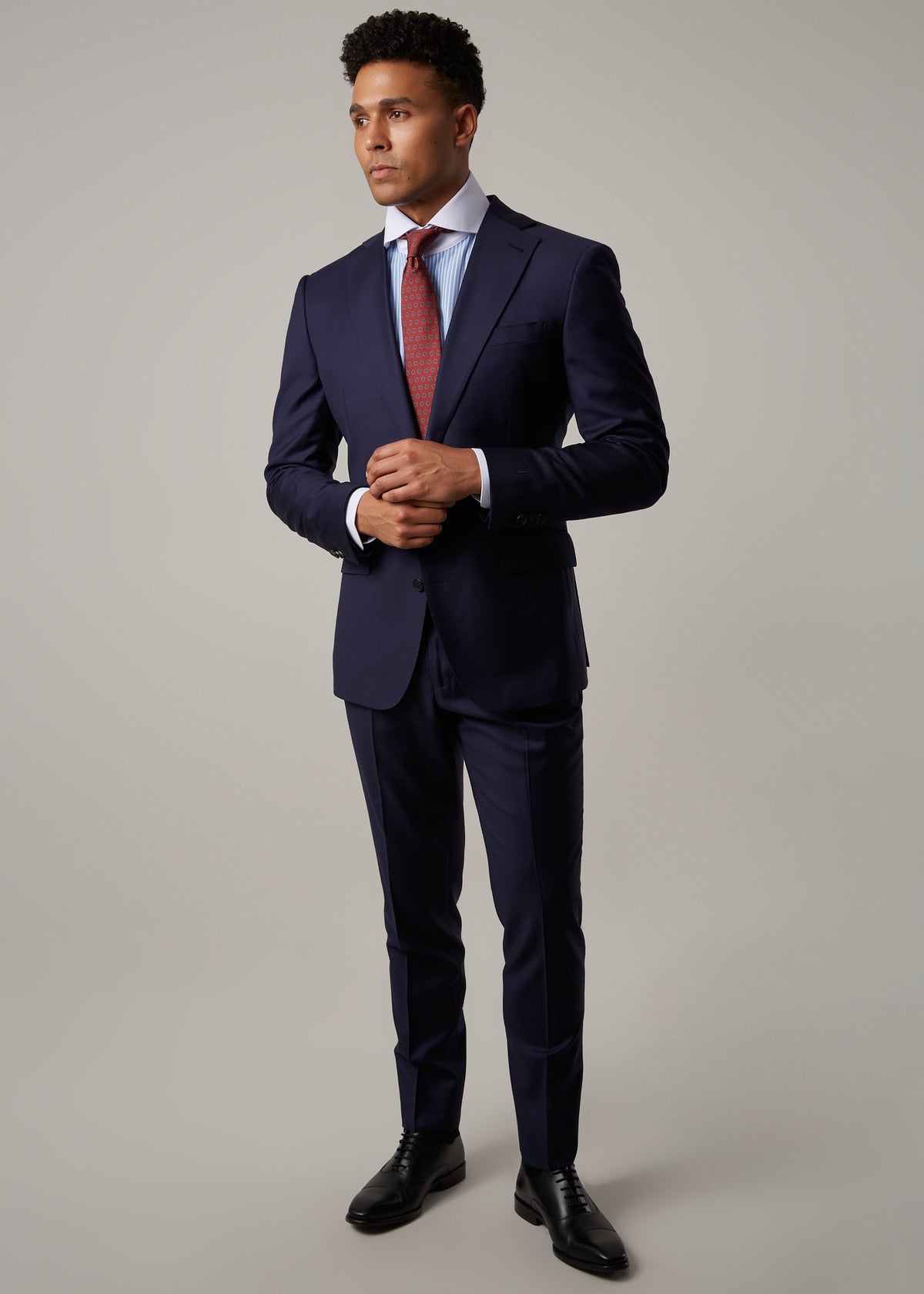Rialto Royale Navy Suit worn with a rust tie, hands clasped, model looking aside