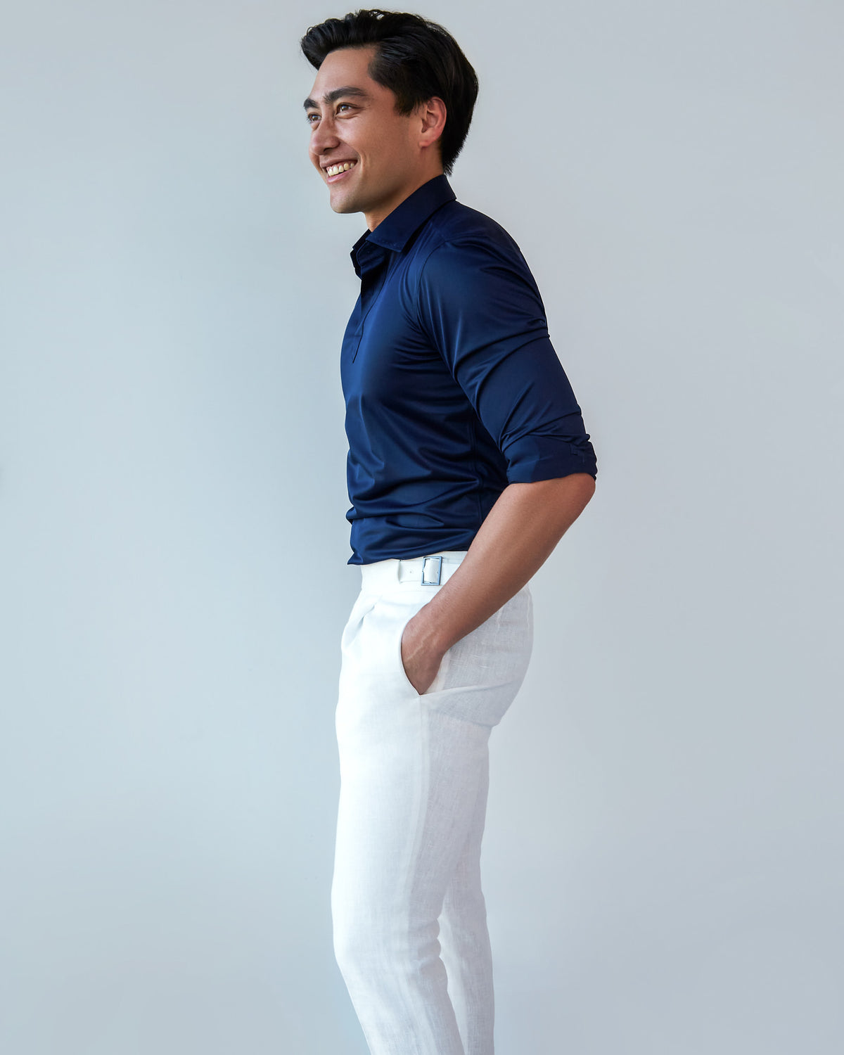 Navy Popover Shirt, side profile with sleeves rolled and a model smiling, white trousers